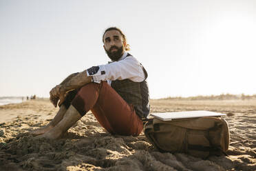 Gut gekleideter Mann sitzt am Strand und schaut sich um - JRFF03630