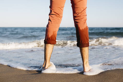 Rückansicht eines Mannes mit orangefarbener Hose, der an einem Strand am Wasser steht, lizenzfreies Stockfoto