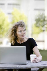 Porträt einer reifen Geschäftsfrau mit Laptop und Kaffee zum Mitnehmen im Freien - KNSF06187