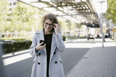 Lächelnde reife Geschäftsfrau mit Blick auf ihr Smartphone - KNSF06193