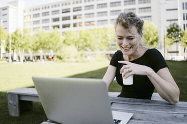 Portrait of smiling mature businesswoman with laptop and coffee to go outdoors - KNSF06194