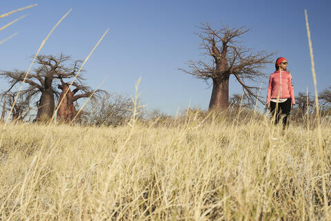 Frau mit Baobab-Bäumen im Hintergrund, Makgadikgadi-Pfannen, Botsuana, lizenzfreies Stockfoto