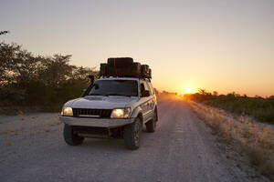 Off-road vehicle driving on a dirt road at sunrise, Makgadikgadi Pans, Botswana - VEGF00491