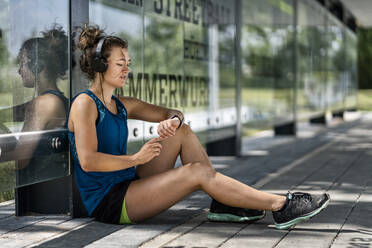 Junge sportliche Frau, die Kopfhörer trägt und ihre Smartwatch überprüft - STSF02187