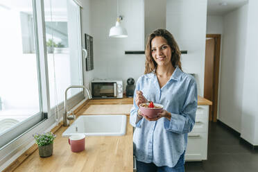 Porträt einer jungen Frau im Pyjama, die zu Hause in der Küche Müsli isst - KIJF02529