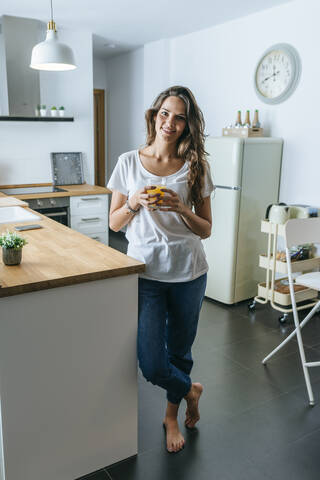 Porträt einer lächelnden jungen Frau, die in der Küche Orangensaft trinkt, lizenzfreies Stockfoto