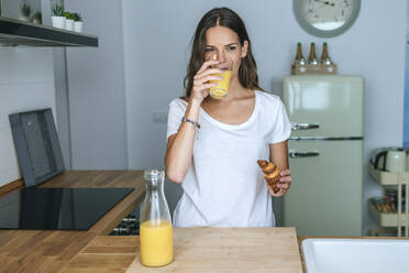 Junge Frau beim Frühstück mit Saft und Croissant in der Küche - KIJF02559