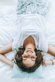 Top view of happy young woman lying in bed with closed eyes - KIJF02576