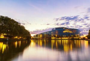 Beleuchtetes Louise-Weiss-Gebäude am Fluss gegen den Himmel bei Sonnenuntergang, Strasbourg, Frankreich - JUNF01733