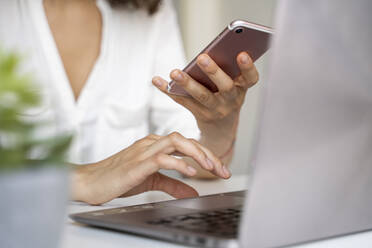 Close-up of woman using cell phone and laptop at desk - AFVF03714