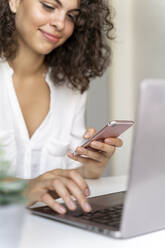 Close-up of woman using cell phone and laptop at desk - AFVF03715