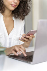 Close-up of woman using cell phone and laptop at desk - AFVF03716