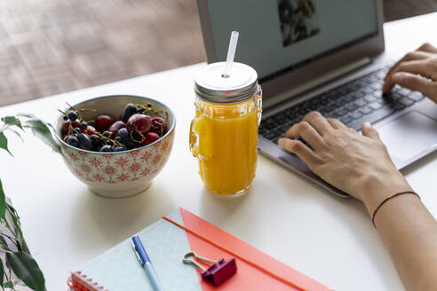 Nahaufnahme einer Frau mit Laptop am Schreibtisch mit Orangensaft und Obst - AFVF03719