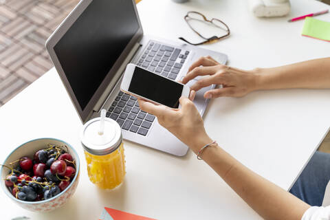 Close-up of woman using cell phone and laptop at desk with orange juice and fruit stock photo