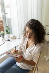 Junge Frau macht sich Notizen am Schreibtisch zu Hause - AFVF03727