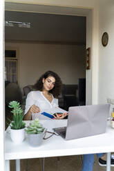 Young woman with notepad and laptop at desk at home - AFVF03729