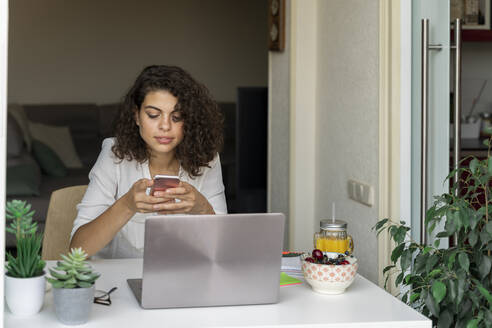 Junge Frau benutzt Handy und Laptop am Schreibtisch - AFVF03733