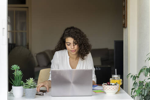 Junge Frau benutzt Handy und Laptop am Schreibtisch - AFVF03734