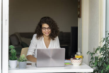Smiling young woman using laptop at desk - AFVF03735