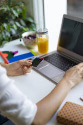 Close-up of woman using laptop and card at desk - AFVF03741