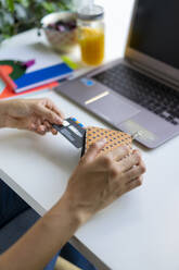 Close-up of woman with laptop taking card out of purse at desk - AFVF03742