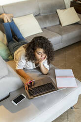 Junge Frau liegt zu Hause auf der Couch und benutzt einen Laptop - AFVF03760