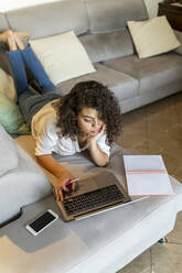 Young woman lying on couch at home using laptop - AFVF03760