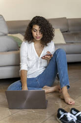 Young woman using cell phone and laptop at home - AFVF03761