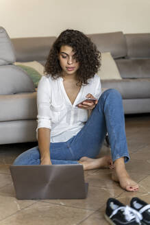 Junge Frau benutzt Handy und Laptop zu Hause - AFVF03761