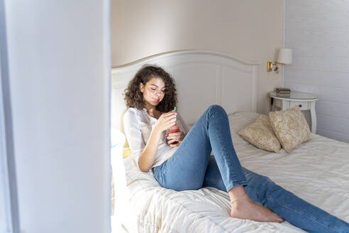 Entspannte junge Frau auf dem Bett liegend mit gesundem Getränk - AFVF03773