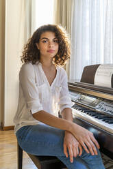 Portrait of young woman sitting at the piano at home - AFVF03778