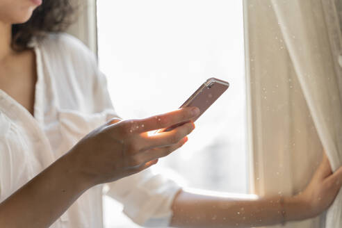 Close-up of woman using cell phone at the window at home - AFVF03784