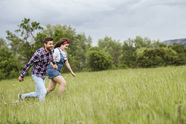 Junges Paar läuft händchenhaltend über ein Feld - LJF00629