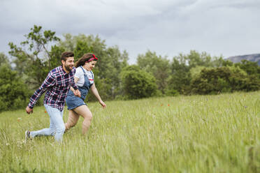 Young couple running over a field holding hands - LJF00629