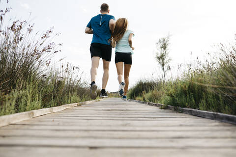 Rückansicht eines jungen Paares beim Joggen auf einem Holzsteg, lizenzfreies Stockfoto