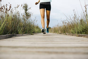 Female jogger running on wooden walkway - JRFF03646