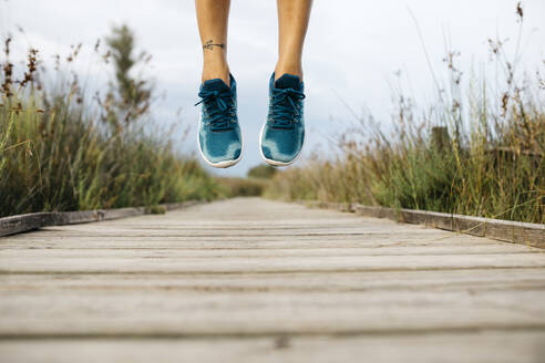 Feet of female jogger, jumping on a wooden walkway - JRFF03648