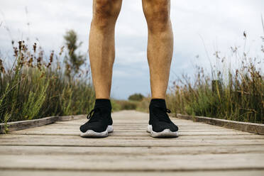 Schwarze Laufschuhe, männlicher Jogger auf einem Holzsteg stehend - JRFF03654