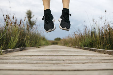 Schwarze Laufschuhe, männlicher Jogger, der auf einen Holzsteg springt, lizenzfreies Stockfoto