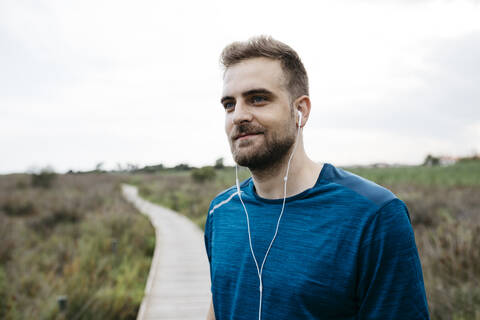 Jogger mit Kopfhörern auf einem Holzsteg stehend, lizenzfreies Stockfoto