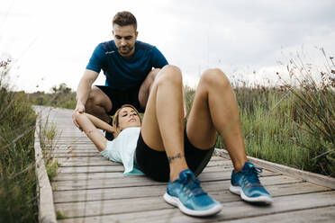 Joggerin trainiert mit ihrem Trainer auf einem Holzsteg, Sit-ups - JRFF03666