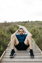 Jogger doing sit-ups on a wooden walkway - JRFF03667