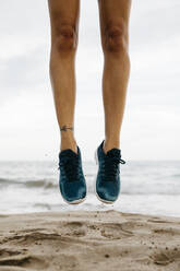 Legs of woman jumping on the beach while training - JRFF03683