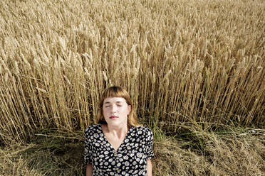 Porträt einer jungen Frau mit geschlossenen Augen, die sich vor einem Getreidefeld entspannt - FLLF00269
