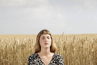 Porträt einer jungen Frau mit geschlossenen Augen, die sich vor einem Getreidefeld entspannt - FLLF00272