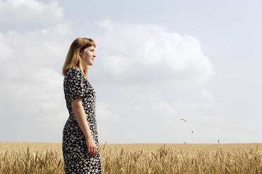 Junge Frau in Kleid mit Blumenmuster in einem Getreidefeld stehend - FLLF00273