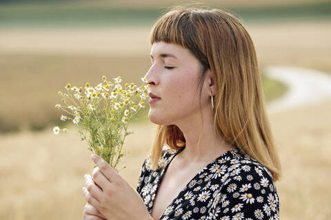 Junge Frau mit geschlossenen Augen riecht an einem Strauß Kamillenblüten, lizenzfreies Stockfoto
