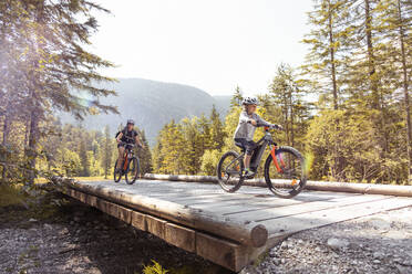 Mother and daughter riding e-mountain bikes in the mountains - FKF03531