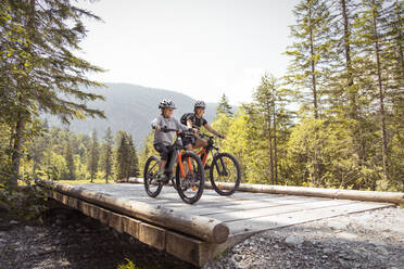 Mother and daughter riding e-mountain bikes in the mountains - FKF03532