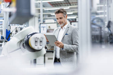 Businessman with tablet at assembly robot in a factory - DIGF07803